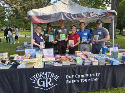 Great Lakes Ford team members holding up children's books at the StorytimeGR table in the park