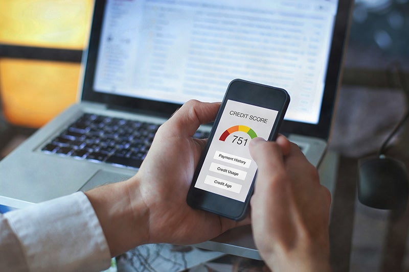 A person checking their credit score on a smartphone next to a laptop