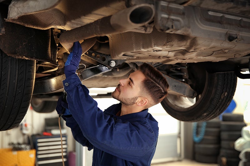 A service technician inspecting the underside of a vehicle on a lift in a service bay