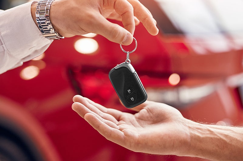 A set of vehicle keys being handed from one person to another beside a car